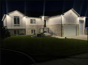 View of front facade featuring board and batten siding, stone siding, a yard, and concrete driveway