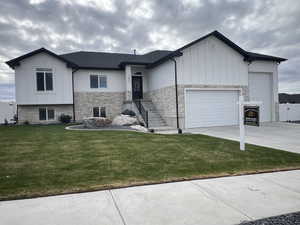 View of front of home with stone siding, board and batten siding, a front yard, and driveway