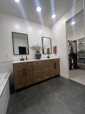 Full bathroom featuring double vanity, dark tile patterned floors, a bath, recessed lighting, and a walk in closet