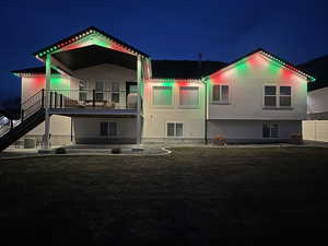 Back of house at twilight featuring stucco siding, stairway, a patio area, and a lawn