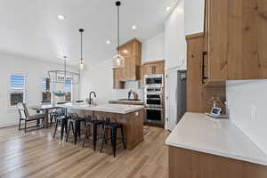Kitchen with brown cabinets, an island with sink, decorative backsplash, pendant lighting, and a breakfast bar