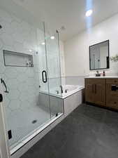 Full bath featuring a shower stall, a bath, vanity, and dark tile patterned floors