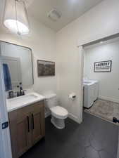 Half bathroom featuring vanity, washing machine and dryer, and dark tile patterned floors