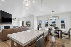 Kitchen with pendant lighting, light wood-type flooring, a fireplace, a kitchen island with sink, and recessed lighting