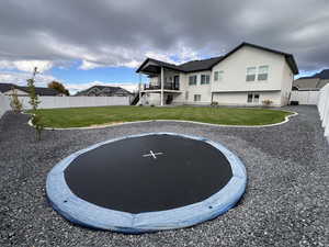 Back of house with a fenced backyard, stucco siding, a trampoline, and a balcony
