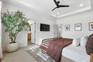 Carpeted bedroom with a raised ceiling, ceiling fan, ensuite bath, and recessed lighting