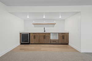 Indoor wet bar featuring brown cabinets, beverage cooler, recessed lighting, and light wood-type flooring