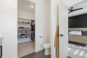 Full bathroom with dark tile patterned floors, dark carpet, a walk in closet, ceiling fan, and vanity
