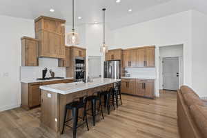 Kitchen featuring backsplash, pendant lighting, brown cabinets, a breakfast bar, and a towering ceiling