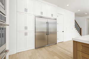 Kitchen featuring built in appliances, recessed lighting, light wood-style flooring, white cabinets, and light stone countertops