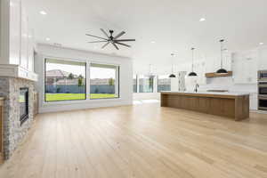 Unfurnished living room featuring a fireplace, light wood-style flooring, recessed lighting, a chandelier, and ceiling fan