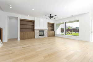 Unfurnished living room with built in shelves, recessed lighting, a fireplace, light wood-type flooring, and a ceiling fan