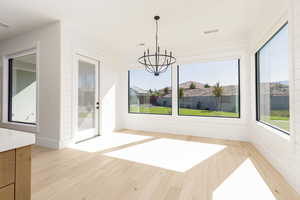 Unfurnished dining area featuring light wood-style floors, plenty of natural light, a chandelier, and wood walls