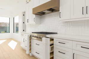 Kitchen featuring white cabinetry, under cabinet range hood, light stone counters, and stainless steel gas stovetop