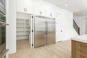 Kitchen featuring built in appliances, recessed lighting, light wood-style flooring, and white cabinets