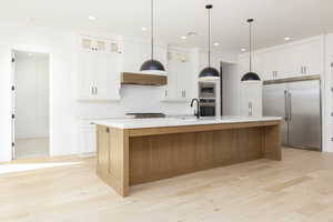 Kitchen with built in appliances, brown cabinets, white cabinets, an island with sink, and recessed lighting