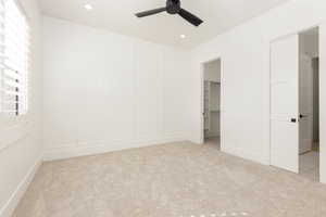 Unfurnished bedroom with a walk in closet, light carpet, a ceiling fan, recessed lighting, and a decorative wall