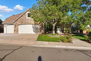 View of property hidden behind natural elements featuring concrete driveway, stone siding, a front lawn, a garage, and a porch