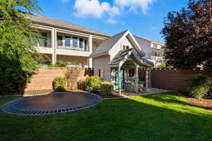 Back of property with a trampoline, stucco siding, a balcony, and a shingled roof
