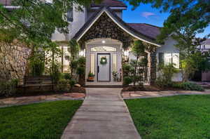 Exterior entry at dusk featuring stone siding, a yard, and stucco siding
