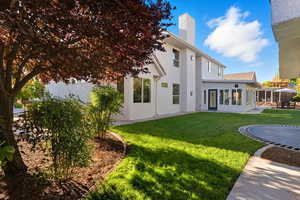 Rear view of property with a yard, a chimney, a sunroom, a patio, and stucco siding