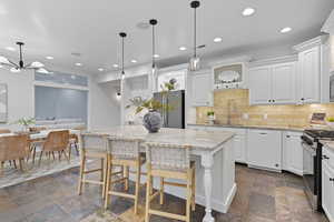Kitchen with hanging light fixtures, backsplash, light stone countertops, white cabinetry, and recessed lighting