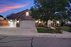 View of front facade with concrete driveway, an attached garage, a front yard, stone siding, and a tiled roof