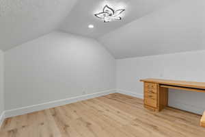 Bonus room with a textured ceiling, lofted ceiling, and light wood finished floors