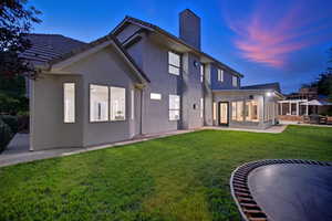 Rear view of property with a lawn, stucco siding, a chimney, and a patio area