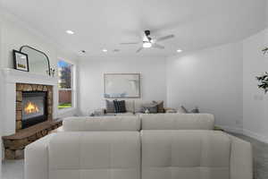 Living area with light colored carpet, ornamental molding, a stone fireplace, a ceiling fan, and recessed lighting