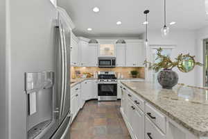 Kitchen with appliances with stainless steel finishes, tasteful backsplash, light stone counters, white cabinets, and recessed lighting