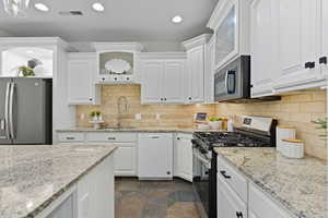 Kitchen featuring appliances with stainless steel finishes, light stone counters, white cabinetry, backsplash, and recessed lighting