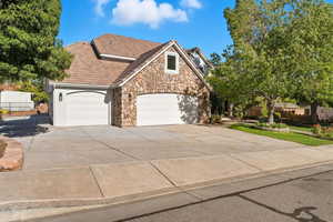 View of front of property with stone siding, driveway, a garage, and stucco siding