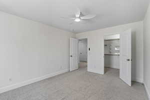 Unfurnished bedroom with a walk in closet, light colored carpet, and a ceiling fan