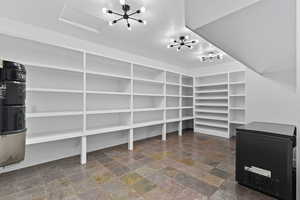 Walk in closet with a chandelier and stone finish floors