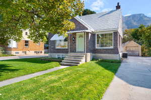 View of front of property with an outbuilding, a detached garage, brick siding, a chimney, and a front lawn