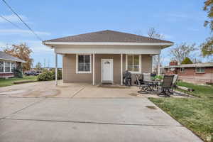 Rear view of house featuring roof with shingles, a lawn, and covered porch