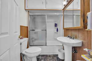 Full bath featuring bath / shower combo with glass door and wooden walls