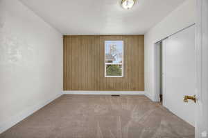 Unfurnished bedroom with wood walls, light carpet, and a closet