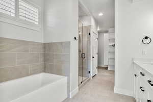 Full bathroom featuring vanity, a bath, a stall shower, a walk in closet, and light tile patterned flooring