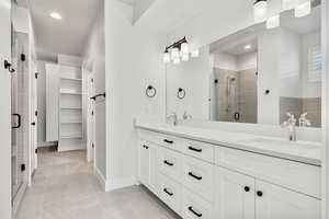 Bathroom featuring a shower stall, a walk in closet, double vanity, recessed lighting, and light tile patterned floors