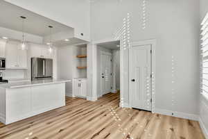 Kitchen featuring white cabinetry, appliances with stainless steel finishes, decorative light fixtures, open shelves, and a high ceiling