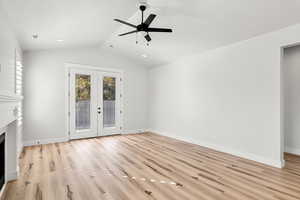 living room featuring french doors, vaulted ceiling, light wood-style floors, a premium fireplace, and ceiling fan