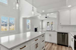 Kitchen featuring white cabinetry, stainless steel dishwasher, plenty of natural light, pendant lighting, and vaulted ceiling