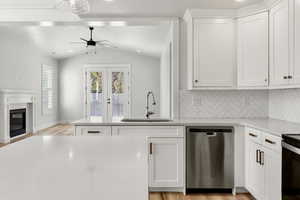 Kitchen with stainless steel dishwasher, tasteful backsplash, white cabinets, light wood-style floors, and vaulted ceiling