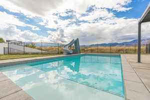 Heated saltwater pool with Baja shelf, cyclone slide, concrete pool deck, and wrought-iron fence for added safety.