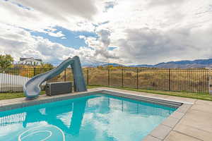 Heated saltwater pool with Baja shelf, cyclone slide, concrete pool deck, and wrought-iron fence for added safety.