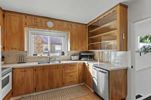 Kitchen with stainless steel appliances, light countertops, brown cabinets, light wood-style flooring, and a wainscoted wall