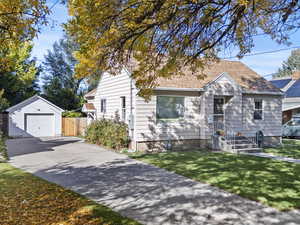 View of front of house featuring an outbuilding, driveway, a detached garage, and a shingled roof
