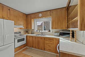 Kitchen featuring white appliances, light countertops, brown cabinetry, and tasteful backsplash